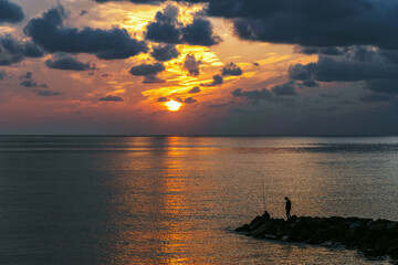 Wall Mural - A calm sea with a sunset sky and the sun through the clouds. Calm seascape. Colorful sunset on the Black Sea. Sea breakwaters. Seascape at sunset under a cloudy sky.