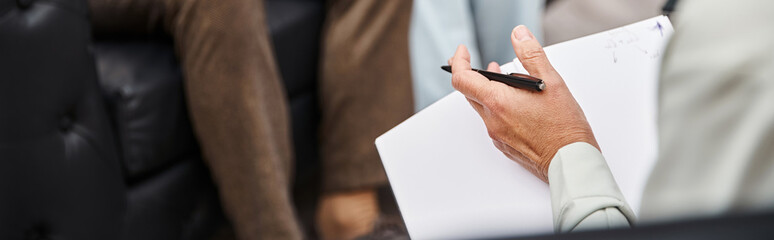 focus on psychologist  holding pen and blank notebook near married couple during appointment, banner