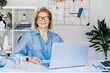 Smiling mature businesswoman with laptop at her office workplace, confident middle-aged experienced senior female professional, CEO of company looking at camera. Female entrepreneur manage business