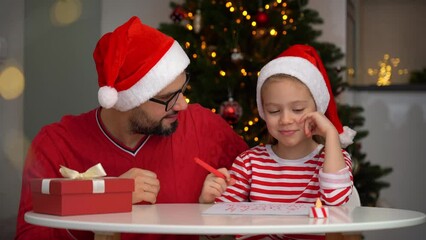 Wall Mural - Father and little daughter write letter to Santa Claus on background of Christmas tree. Happy family discuss about what gift to wish for New Year