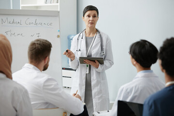 Wall Mural - Waist up portrait of senior female doctor presenting to audience at medical conference, copy space