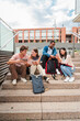 © Jose Calsina - Vertical. Group of multiracial high school students talking on a staircase at university campus, using a tablet app and smartphone to do homework project after class. Friendly teenage people studying