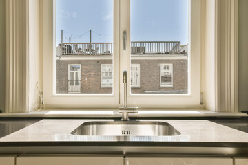 Wall Mural - a kitchen sink in front of a window with the view of a brick building and blue sky through the windows