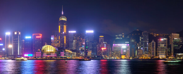 Panorama of Hong Kong skyline cityscape downtown skyscrapers over Victoria Harbour in the evening illuminated tourist boats and ferries . Hong Kong, China