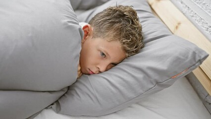 Wall Mural - Adorable blond boy, comfortable and cozy in pajamas, lying on bed with serious expression, awakening to a relaxed morning in his bedroom.