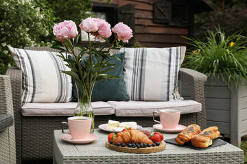 Canvas Print - Morning drink, pastry, berries, cheese and vase with flowers on rattan table. Summer breakfast outdoors