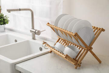 Canvas Print - Drying rack with clean dishes on light marble countertop near sink in kitchen