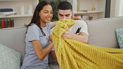 Sticker - Beautiful couple in love, resting comfortably and smiling while watching a movie on tv, sitting together on their sofa in the living room of their cozy home