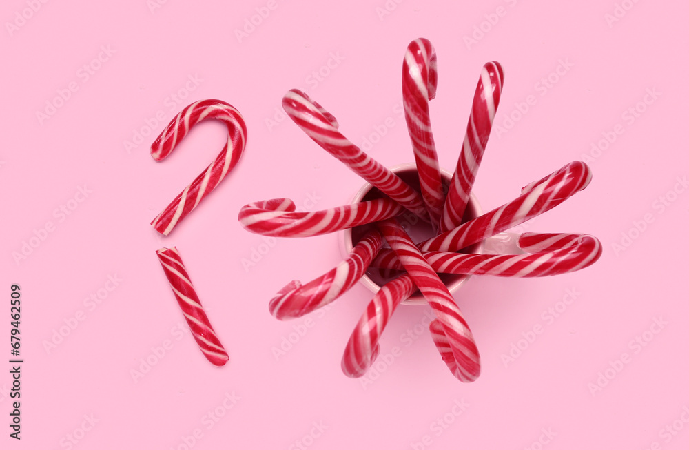 Cup with Christmas candy canes on pink background