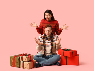 Sticker - Surprised young couple with Christmas tinsel and gift boxes on pink background