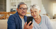 © Azeemud/peopleimages.com - Senior couple, smartphone and video call in living room sofa, conversation and joyful. Grandparents, technology and communication with family, man and woman in retirement, happy and connection