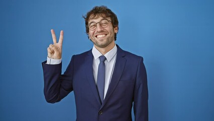 Sticker - Cheerful young man in formal business suit happily pointing up, showing number two with fingers. a beaming smile across his face against isolated blue background.