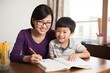 © Stavros - Mom helps son do homework sitting at table writing in notebook right answer. Asian boy asks mother to help with homework at table with laptop. Mom in cozy modern apartment helps her son with lessons
