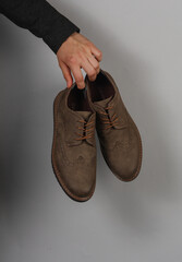 Wall Mural - Man's hand holding brogue boots on gray background