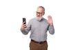 a gray-haired mature man with a beard and mustache in trousers and a shirt takes a selfie on the phone