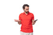young handsome man with black hair and beard dressed in a red t-shirt throws up his hands using a smartphone