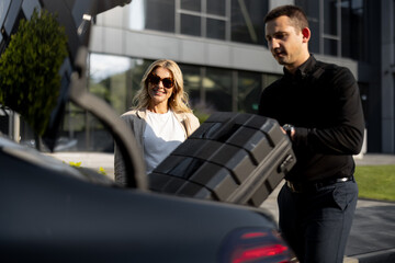 Wall Mural - Businesswoman waits while chauffeur packs a suitcase in car trunk, using luxury taxi service during a business trip. Concept of business transfer services, idea of personal driver.