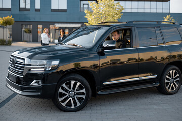 Wall Mural - Man drives luxury black SUV vehicle near an office building, side view. Big boss concept