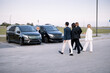 Group of an elegant business people walk together to minivan taxies on a parking lot. Concept of transfer service and business