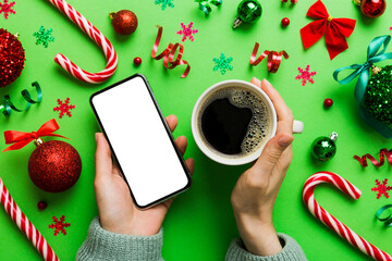 Wall Mural - Above view of female hand holding smart phone with hot cup of coffee. Christmas decoration on colored background