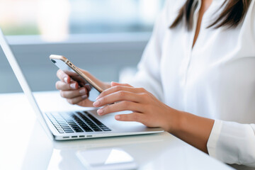  woman uses a cell phone while using laptop keyboard on white table