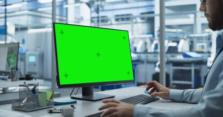 Fototapete - Young Industrial Software Engineer Working on a Desktop Computer with Green Screen Mock-Up Display. Modern Factory with High-Tech Machinery and Robotic Arms in the Assembly Hall
