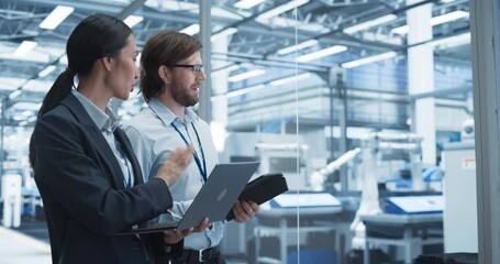 Poster - Two Multiethnic Engineers Standing in Office, Using Laptop and Tablet Computers at an Electronics Factory. Machines are Undergoing Maintenance, Specialists Monitoring the Progress on Devices