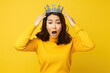 Portrait of worried puzzled Asian woman touching her brilliant crown, staring at camera with terrified face isolated on yellow color background.