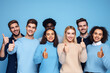Young people with approving expression looking at camera showing success and like gesture on blue background. Diverse happy multiracial people holding raised thumbs ups.