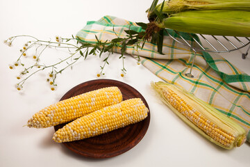 Clay plate with two cobs sweet corn on white wooden background..