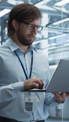 Aufkleber - Vertical Screen: Portrait of a Handsome Engineer with Glasses Using Laptop Computer and Looking Around a Factory Facility with Equipment Producing Modern Electronic Components for Different Industries