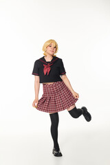 Wall Mural - jolly young woman in school uniform posing on one leg on white, youthful cosplay subculture