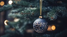  A Blue Christmas Ornament Hanging From A Christmas Tree With Lights In The Backgrounnd Of It.