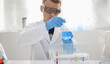 © H_Ko - A male chemist holds test tube of glass in his hand overflows a liquid solution of potassium permanganate. Conducts an analysis reaction takes various versions of reagents using chemical manufacturing