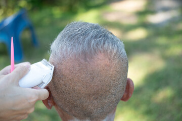 An elderly Asian person gets his hair cut outdoors.