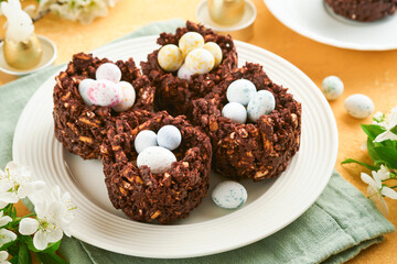 Wall Mural - Easter chocolate nest cake with mini chocolate candy eggs with blossoming cherry or apple flowers on yellow background table. Creative recipe for Easter table with holiday decorations. Top view.