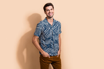 Wall Mural - Photo of good mood optimistic man with stylish hairdo dressed print shirt standing keep arms in pockets isolated on beige color background