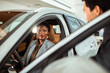 © Marko Geber - Young woman sitting in car looking at salesman in dealership