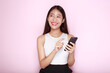 © Parichat - Standing and pointing happily, Portrait of a beautiful young woman in a light pink background, Asian woman holding a phone in one hand.