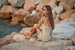 © Евгений Бордовский - Closeup portrait of attractive brunette girl with long hair posing on rocky beach on sunset background. She wears elegant long dress, sunglasses. She is smiling.
