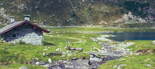 Wall Mural - Mountain landscape. Adventure background. Small stone hut and a little bridge near the lake. Cornisello lake, Val Nambrone, Italy.