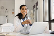© fizkes - Cheerful beautiful young doctor woman in head phones posing at hospital workplace with laptop computer, looking at camera with toothy smile, offering online medical consultation. Professional portrait
