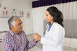 Happy empathetic young doctor touching hand of elderly Indian patient with geriatric diseases, holding arm with support, calming senior man, giving medical care, consultation, smiling, laughing