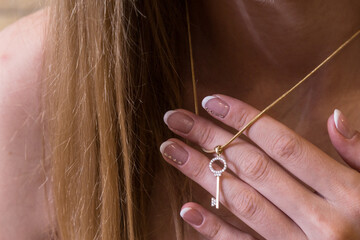 A beautiful girl holds a gold pendant in the form of a key on a gold chain with her fingers