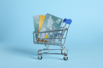 Canvas Print - Small metal shopping cart with credit cards on light blue background