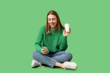 Wall Mural - Beautiful woman with mobile phone and cup of coffee sitting on green background