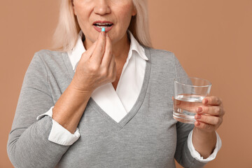 Sticker - Beautiful mature woman with pill and glass of water on brown background