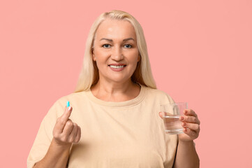 Poster - Beautiful mature woman with pill and glass of water on pink background