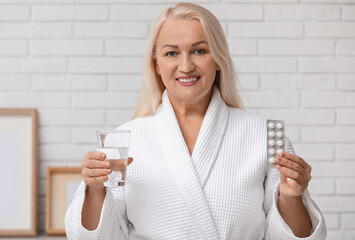 Sticker - Beautiful mature woman with pills and glass of water at home