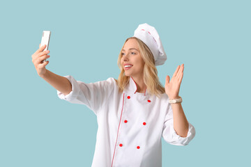 Poster - Beautiful young female chef with mobile phone waving hand on blue background